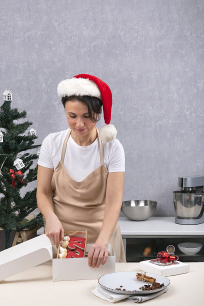 糖果包装礼盒与美味的圣诞糖果。在厨房里戴着新年帽子的女人的肖像。垂直框架图片下载
