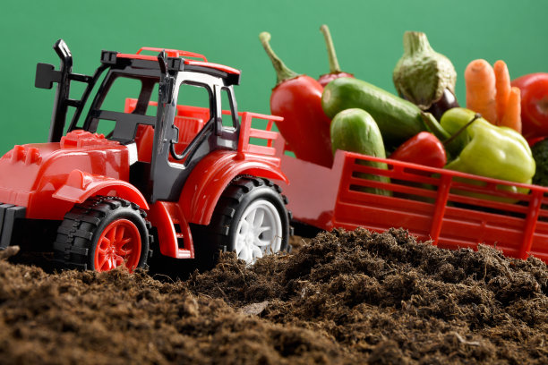 玩具拖拉机载着蔬菜在绿色背景的土壤上图片下载