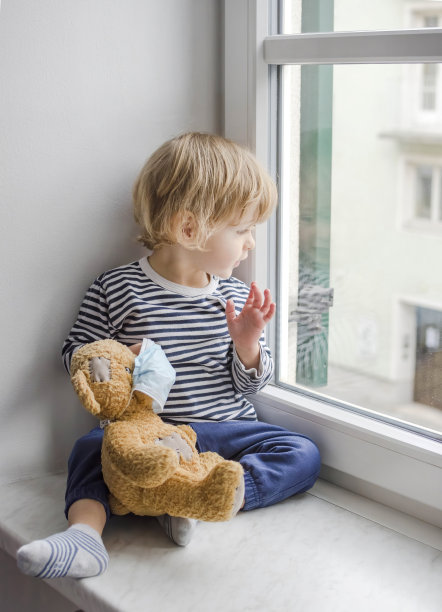 2019冠状病毒和流感封锁期间，居家隔离的孩子戴着医用口罩和生病的泰迪熊望向窗外。有选择性的重点图片下载