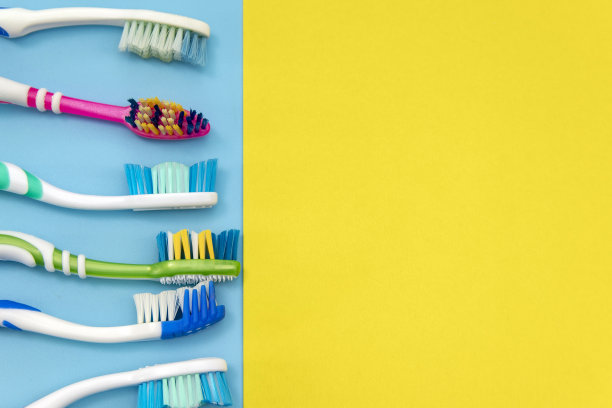 蓝色背景上的多色牙刷。用手牙刷在彩色背景上的平面构图，靠近复制空间。图片下载