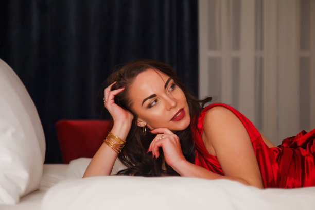 年轻性感漂亮的黑发女人在红色的裙子躺在酒店的床上的特写图片下载