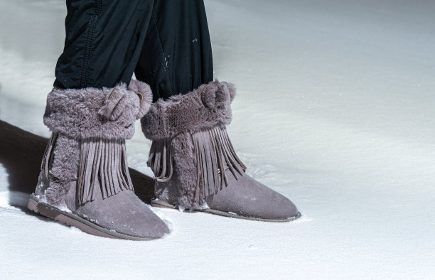 脚上的女性靴子装饰有毛皮和流苏在雪地里。雪地靴靴。图片下载