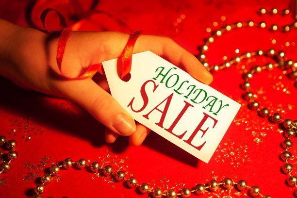 在圣诞节和新年假期期间，一名妇女的手拿着一个白色标签，上面写着“节日促销”，这是装饰过的圣诞背景。图片下载