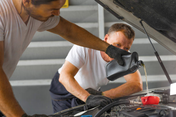 在加油站修理厂修理中心，修理工人正在往发动车上倒机油。概念工厂的设备维修和替换汽车业务行业。图片下载