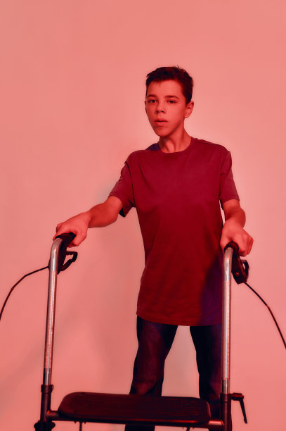 青少年残疾男孩的肖像与脑瘫看向远方，采取步骤与他的步行者孤立在红光背景图片下载