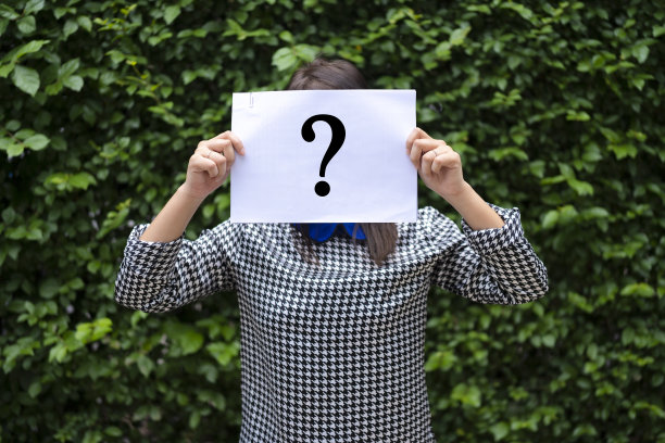 亚洲女人拿着带问号的纸，背景是一扇叶墙。图片下载