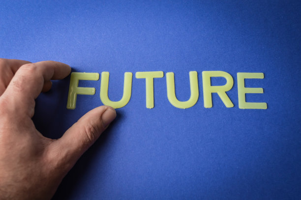 人类的手指拿着一个用塑料字母写在深蓝色纸上的单词“未来”，概念图片下载