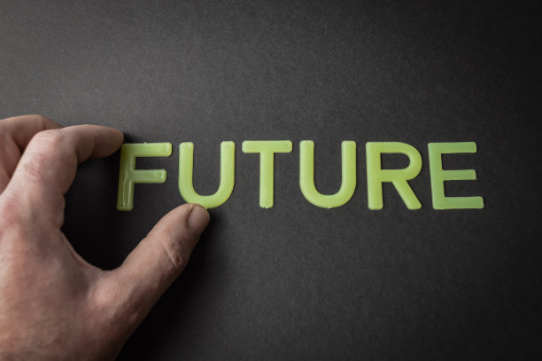 在深灰色的纸上，人们用手指移开塑料字母写的单词“未来”，概念图片下载