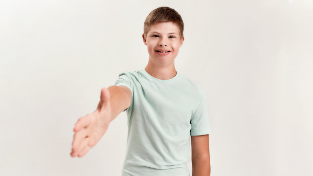 快乐的残疾男孩与唐氏综合症微笑和伸出他的手向相机，在白色背景孤立摆姿势图片下载