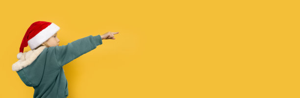 漂亮的小女孩戴着圣诞帽，微笑着指着她的手指。图片下载