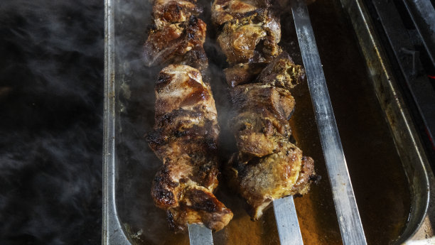 深色背景上，串在烤肉串上烤的烤肉串。前景上散焦的烟雾。街头食品的概念。图片下载