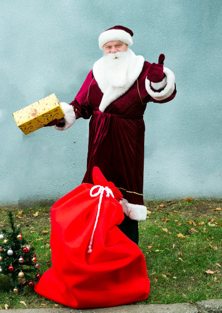 圣诞老人带着一大袋礼物。圣诞老人微笑着向每个人问好。灰色背景和绿色草地的特写。图片下载