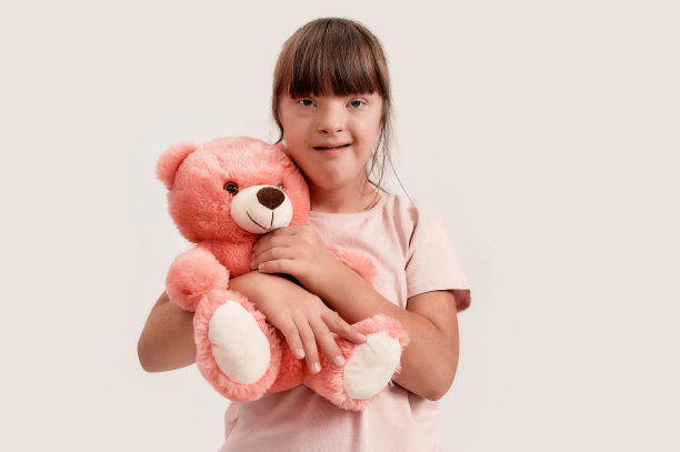 残疾女孩的肖像与唐氏综合症看着相机，抱着她的泰迪熊，而摆出孤立的白色背景图片下载