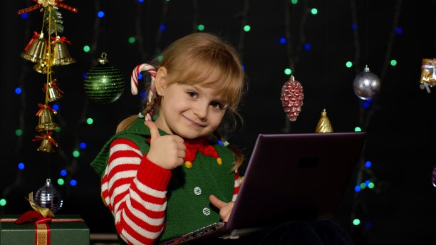 穿着圣诞精灵服装的小女孩在网上购物用笔记本电脑，浏览社交媒体图片下载