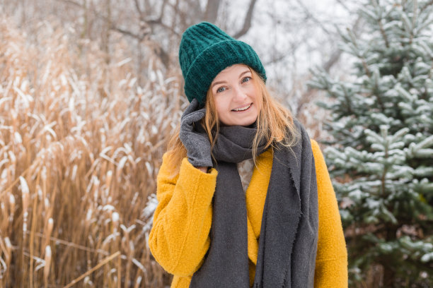快乐的年轻女子穿着外套，帽子和围巾，在自然背景下微笑，2021年的流行颜色-明亮的黄色和终极灰色，冬天的时间图片下载