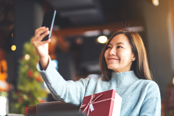一位年轻美丽的亚洲女子用手机与礼盒自拍图片下载