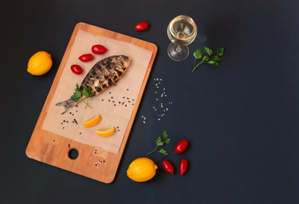 在切菜板上放着美味的烤剑鱼，旁边放着一杯白葡萄酒，柠檬，欧芹和西红柿。图片下载