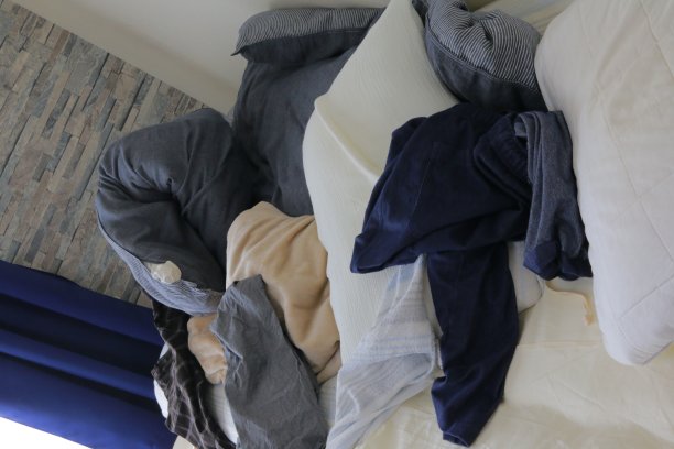 床，羽绒被和枕头在一个肮脏的房间和凌乱的衣服图片下载