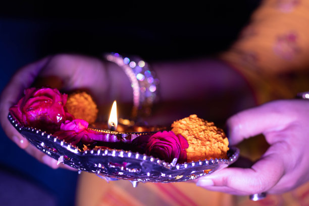 明亮的发光的彩色陶器灯粘土Diya或深在Puja塔利装饰鲜花在晚上在节日庆祝和女性的手在模糊的黑色背景图片下载