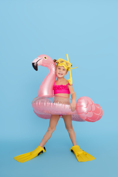 一个穿着泳衣、戴着潜水面罩、脚蹼、戴着充气戒指的快乐女孩要去度暑假了。蓝色背景图片下载