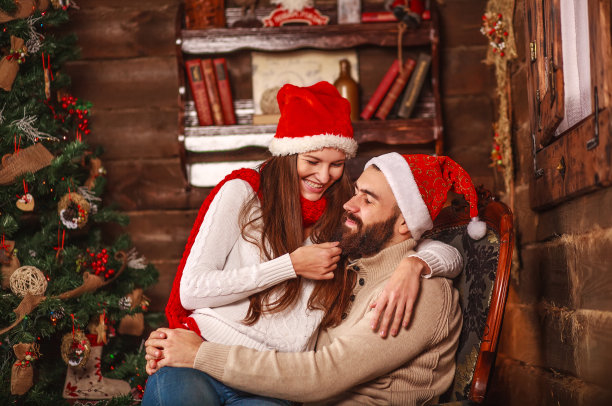 幸福的年轻夫妇戴着圣诞老人的帽子在家拿着新年礼物图片下载