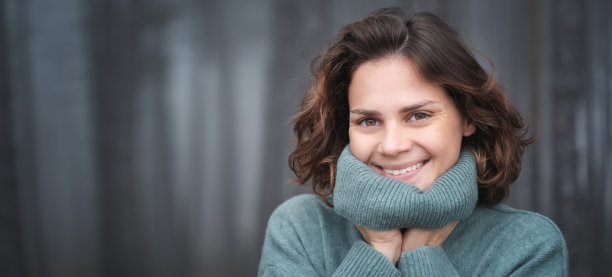 幸福的女人在温暖舒适的绿色毛衣在美丽的雾蒙蒙的松树林图片下载