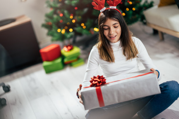 一个女孩坐在地板上，手里拿着一件大圣诞礼物图片下载