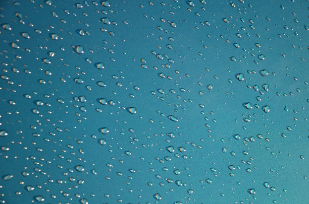 水滴在一辆汽车潮湿的引擎盖上的绿色金属漆上。由于洗车蜡的使用，你不能买到非常漂亮的反光和大的水滴。手工抛光的汽车阳光表面图片下载