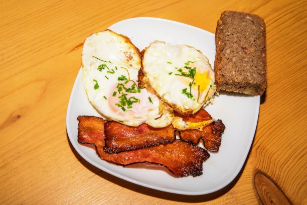 盛有煎蛋、熏肉和面包的盘子放在木桌上。不健康的脂肪类食物。酮饮食图片下载