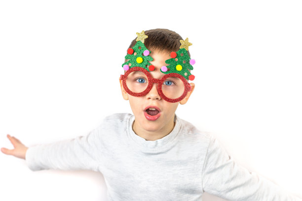 男孩戴着儿童眼镜，带着圣诞树在白色背景下做鬼脸。图片下载