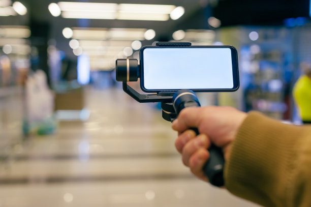 一名男子手里拿着一个稳定剂的智能手机。购物中心的博主。图片下载