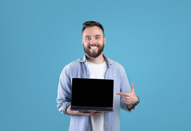 肖像快乐的胡子男人拿着笔记本电脑与空屏幕上的蓝色工作室背景，设计的模型图片下载