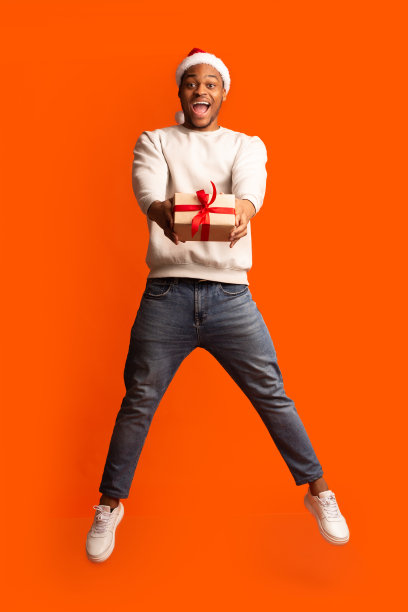 礼物送给你。兴奋的非洲人在圣诞老人帽与礼物跳跃图片下载