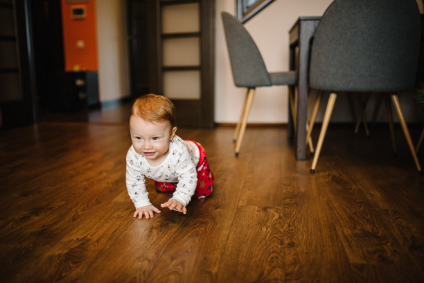 一个小男孩学会在地板上爬，在房间里爬来爬去。现实生活中的蹒跚学步的婴儿在起居室。图片下载