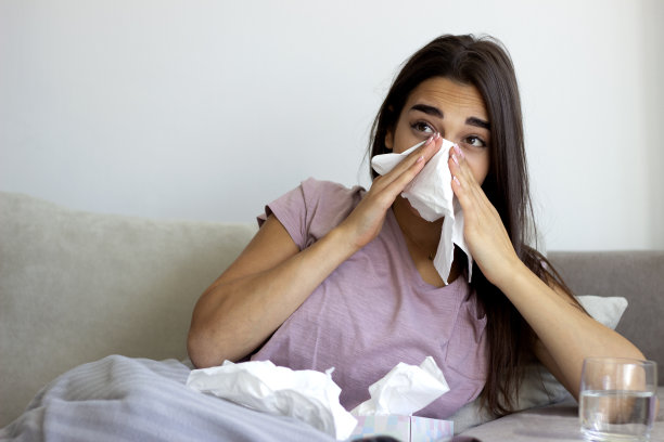 生病的年轻女子因感冒躺在家里的沙发上。图片下载