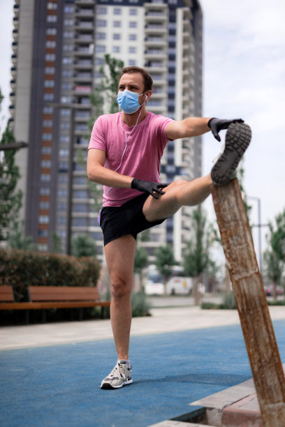 运动员戴着医用口罩和手套，智能手机和耳塞，在城市环境中慢跑。图片下载