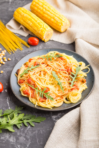 在黑色的混凝土背景和亚麻织物上涂有番茄酱和芝麻菜的玉米面条。侧视图，特写，选择性聚焦。图片下载