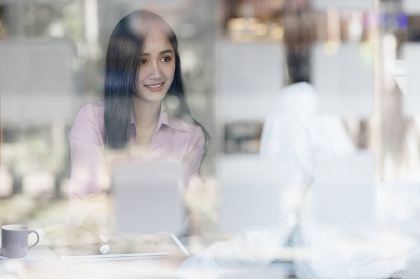 年轻美丽的女人与她的伙伴讨论坐在现代的办公室，透过窗户看。图片下载