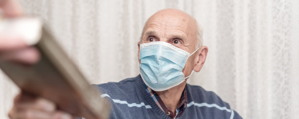 戴着蓝色防护面罩的老人从医院助理那里取书图片下载
