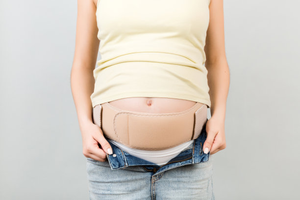 特写孕妇在弹性怀孕绷带，使疼痛消失在灰色背景与复制空间。骨科腹部支撑带概念图片下载