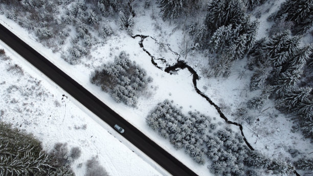 无人机拍摄的一辆汽车在冬天穿过森林的道路图片下载