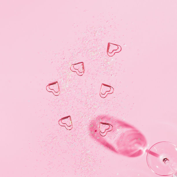 水晶香槟玻璃与心形状的五彩纸屑在柔和的粉红色背景。最小的风格。图片下载