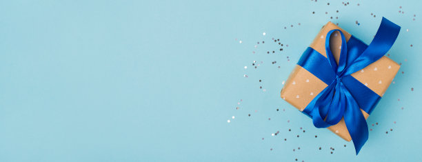 近距离宽照片美丽的礼盒包装在牛皮纸蓝色丝带孤立轻柔和的颜色背景与银色五彩纸屑空空白拷贝空间图片下载