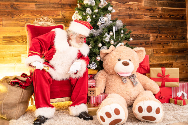 真正的圣诞老人和大泰迪熊坐在圣诞树下。图片下载