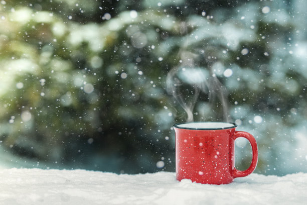 红色的杯子里放着冬天的热饮(热葡萄酒、可可、咖啡、茶)，背景是冬天的森林和积雪。冬天心情舒畅。图片下载
