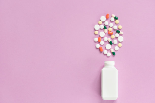 装有杂色药丸的白色药瓶。药品概念保险，药价高。孤立在粉红色的背景上。图片下载