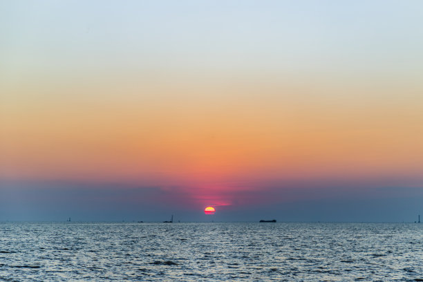 海鸥在美丽的日落背景下飞过海面。图片下载