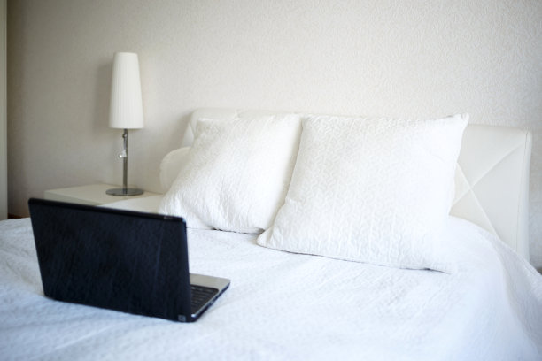 白色卧室，床上放着笔记本电脑。远程工作的概念图片下载
