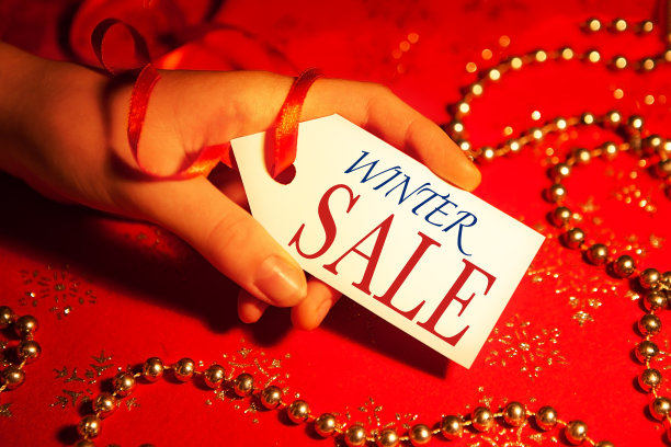 一位女士的手拿着一个标签，上面写着:圣诞节和新年假期期间，装饰过的圣诞背景上的冬季促销。图片下载