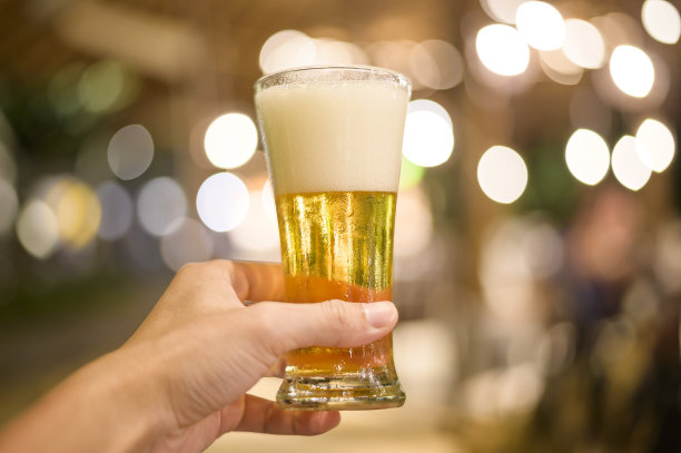 近距离的手拿着一杯啤酒庆祝在餐厅。图片下载